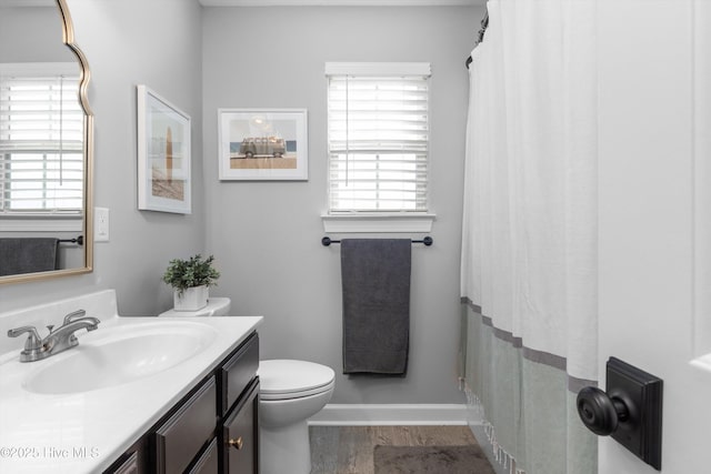 bathroom featuring baseboards, toilet, a shower with shower curtain, wood finished floors, and vanity