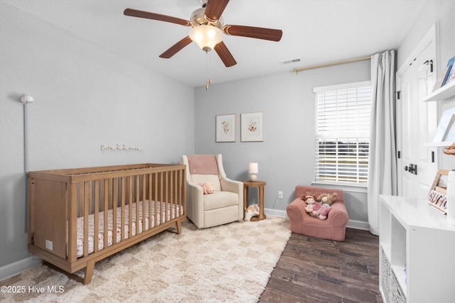 bedroom with visible vents, a crib, baseboards, wood finished floors, and a ceiling fan