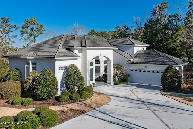 view of front of house with a garage, concrete driveway, a tile roof, and stucco siding