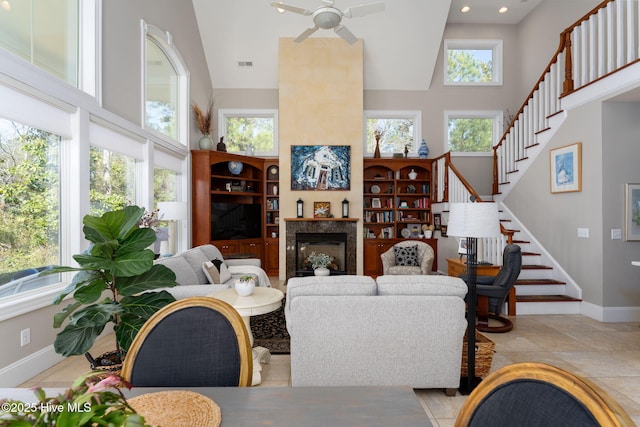 living room featuring stairway, a glass covered fireplace, a towering ceiling, and a healthy amount of sunlight