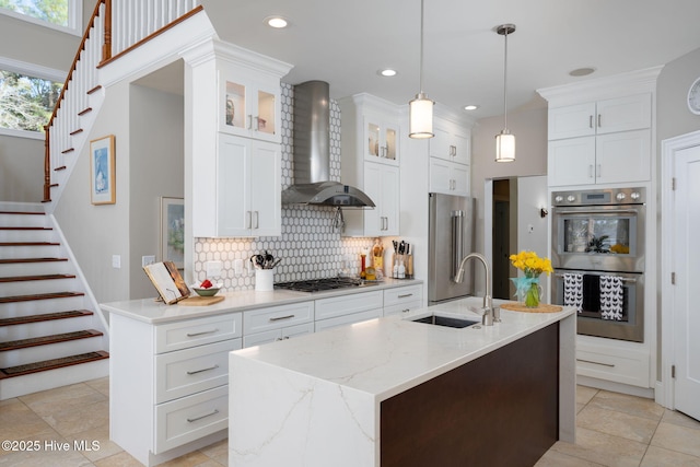 kitchen with a sink, white cabinets, wall chimney range hood, appliances with stainless steel finishes, and backsplash