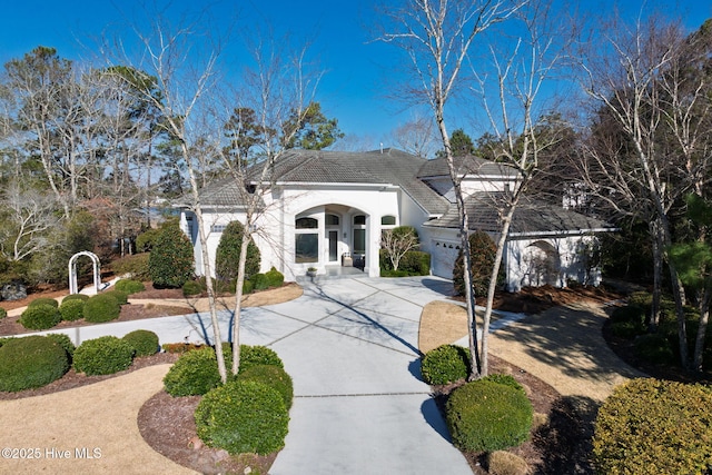 french country home featuring a garage, concrete driveway, a tile roof, and stucco siding