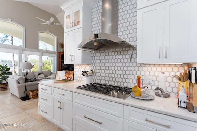 kitchen with white cabinetry, wall chimney range hood, decorative backsplash, glass insert cabinets, and stainless steel gas stovetop