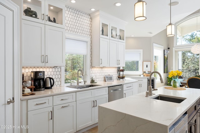 kitchen with stainless steel dishwasher, backsplash, a sink, and a center island with sink