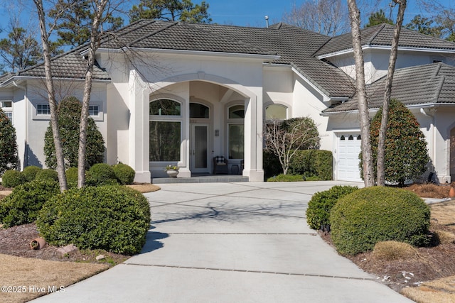 view of exterior entry featuring concrete driveway, an attached garage, a tile roof, and stucco siding