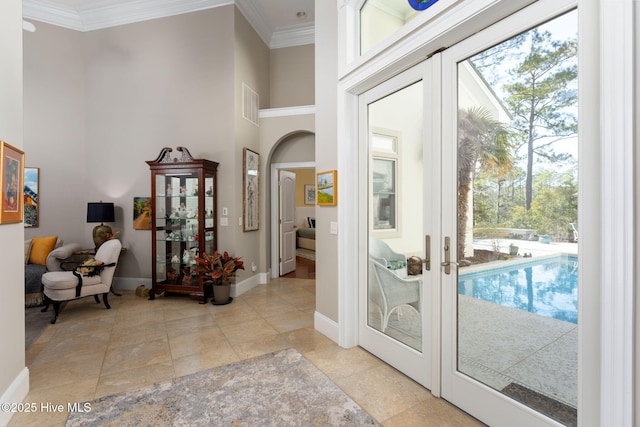 entryway with a towering ceiling, a healthy amount of sunlight, crown molding, and french doors