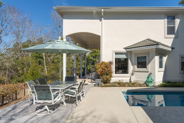 back of property with a tiled roof, fence, an outdoor pool, and stucco siding