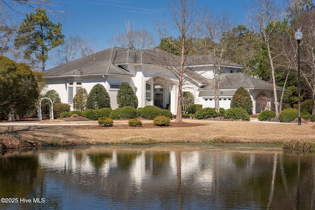 exterior space with a water view, a tile roof, a garage, and stucco siding