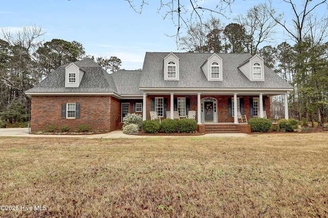 new england style home with a shingled roof, a front yard, brick siding, and a porch