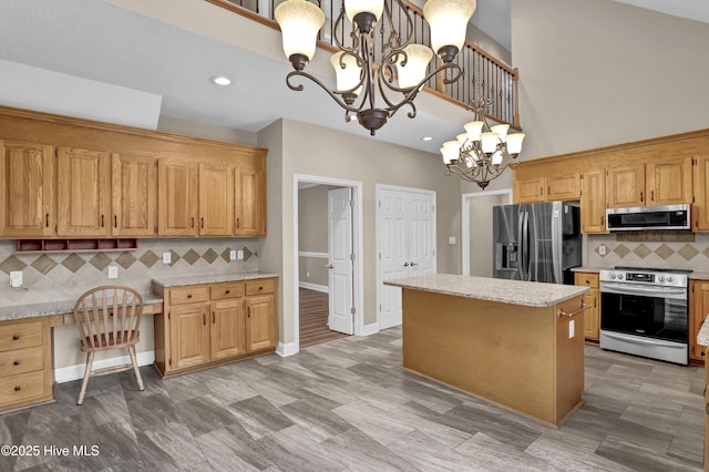 kitchen featuring light stone counters, decorative light fixtures, built in desk, stainless steel appliances, and a chandelier