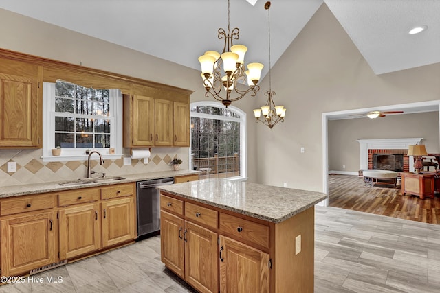 kitchen with light stone counters, a sink, stainless steel dishwasher, a brick fireplace, and decorative backsplash