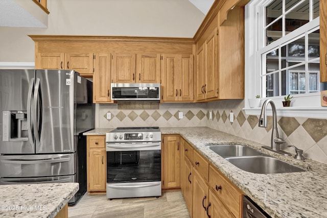 kitchen with a sink, vaulted ceiling, appliances with stainless steel finishes, decorative backsplash, and light stone countertops