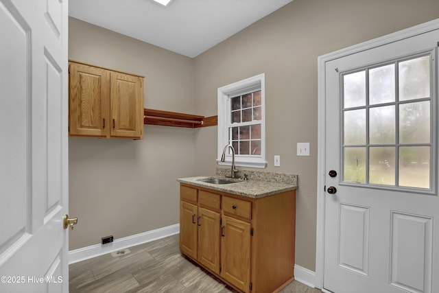 clothes washing area with light wood-type flooring, a sink, and baseboards