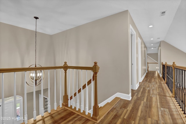 hallway with baseboards, visible vents, wood finished floors, an upstairs landing, and a chandelier