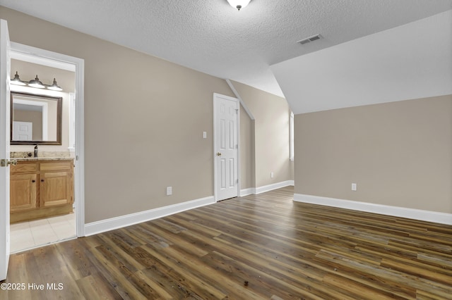 bonus room with vaulted ceiling, a textured ceiling, baseboards, and wood finished floors