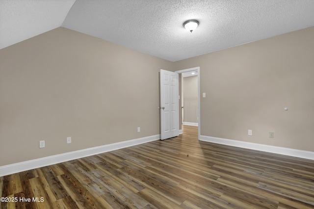 spare room featuring dark wood-style floors, a textured ceiling, lofted ceiling, and baseboards