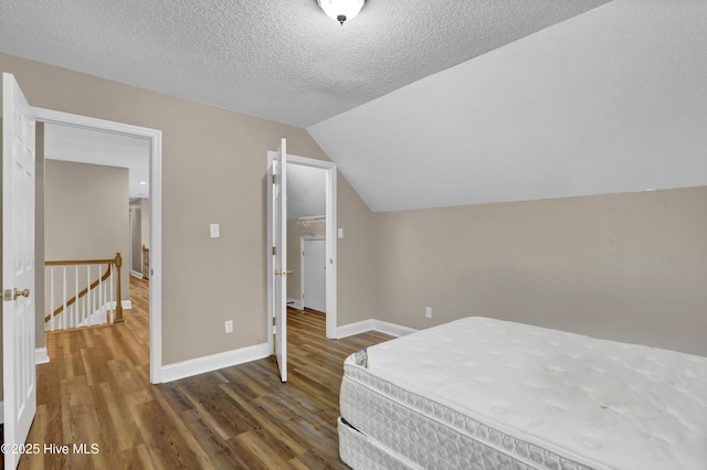 bedroom featuring vaulted ceiling, a textured ceiling, wood finished floors, and baseboards