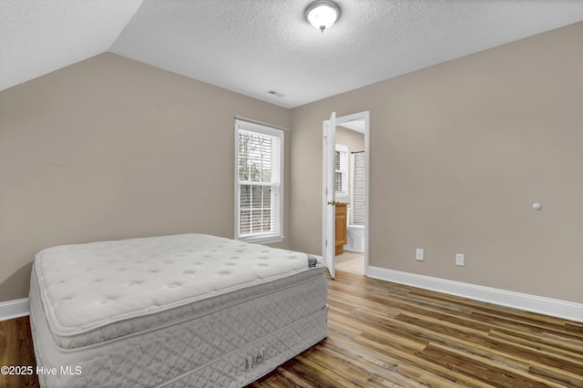 bedroom with a textured ceiling, vaulted ceiling, wood finished floors, and baseboards