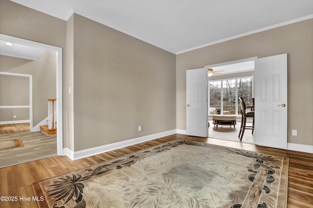 spare room featuring stairs, crown molding, baseboards, and wood finished floors