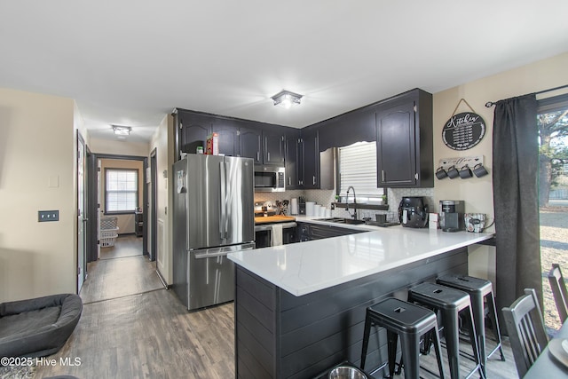 kitchen with a peninsula, a sink, light countertops, appliances with stainless steel finishes, and backsplash