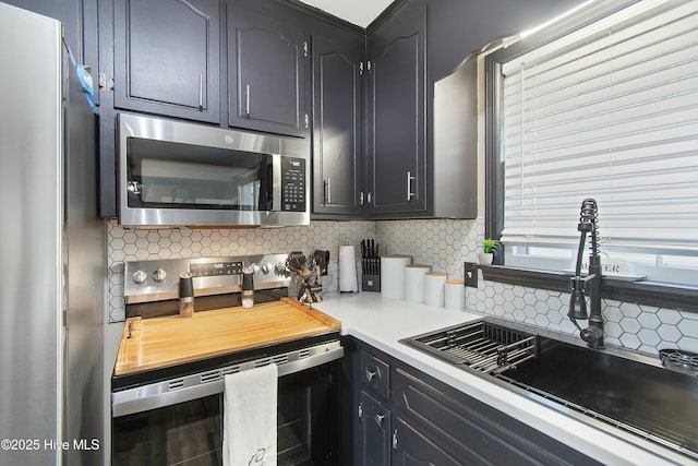 kitchen featuring stainless steel appliances, dark cabinetry, backsplash, and a sink