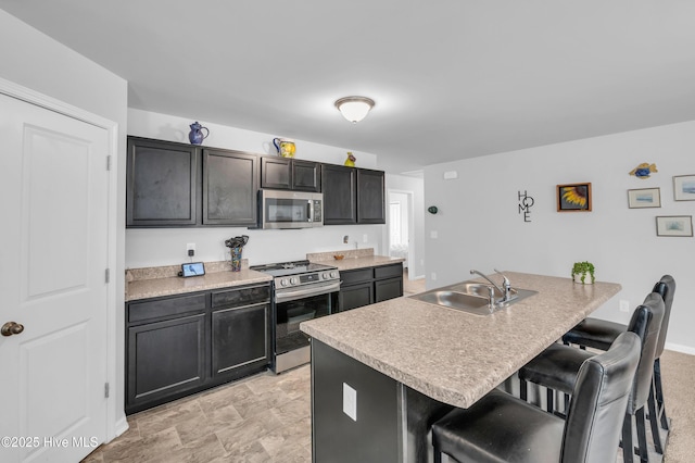 kitchen with a sink, light countertops, a kitchen bar, appliances with stainless steel finishes, and a kitchen island with sink