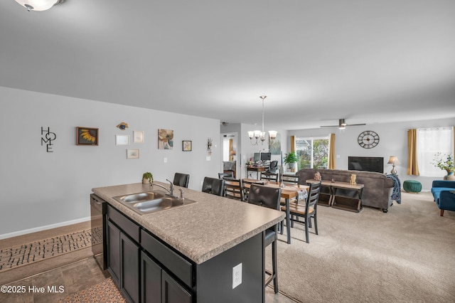 kitchen featuring a breakfast bar area, a kitchen island with sink, a sink, black dishwasher, and open floor plan