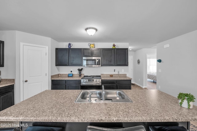 kitchen featuring a kitchen bar, light countertops, appliances with stainless steel finishes, and a sink