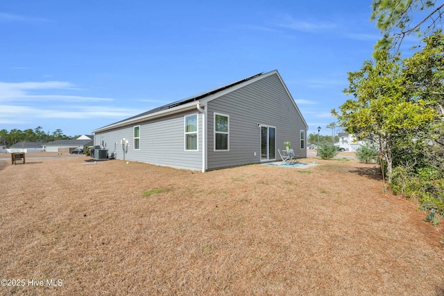 back of house with central air condition unit, a lawn, a patio, and roof mounted solar panels