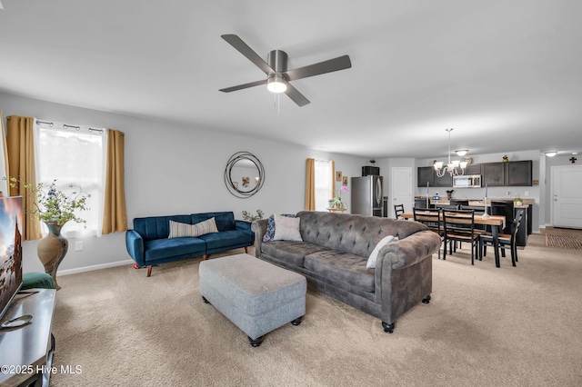 living area with light colored carpet, ceiling fan with notable chandelier, and baseboards