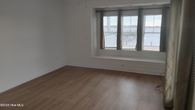 unfurnished room featuring plenty of natural light, baseboards, and wood finished floors