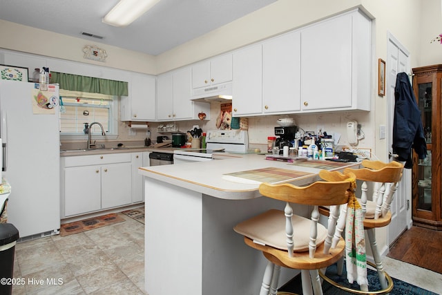 kitchen with white appliances, a peninsula, light countertops, under cabinet range hood, and a sink