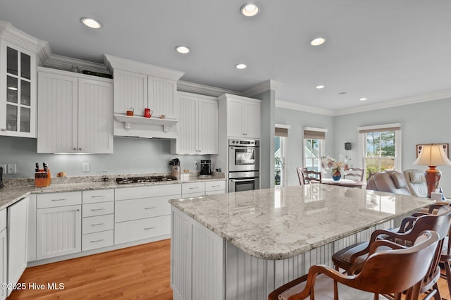 kitchen featuring a kitchen island, white cabinetry, appliances with stainless steel finishes, a kitchen bar, and crown molding