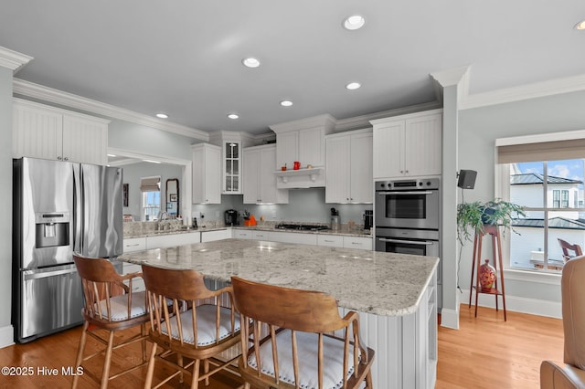 kitchen with light wood finished floors, stainless steel appliances, tasteful backsplash, white cabinetry, and a kitchen island