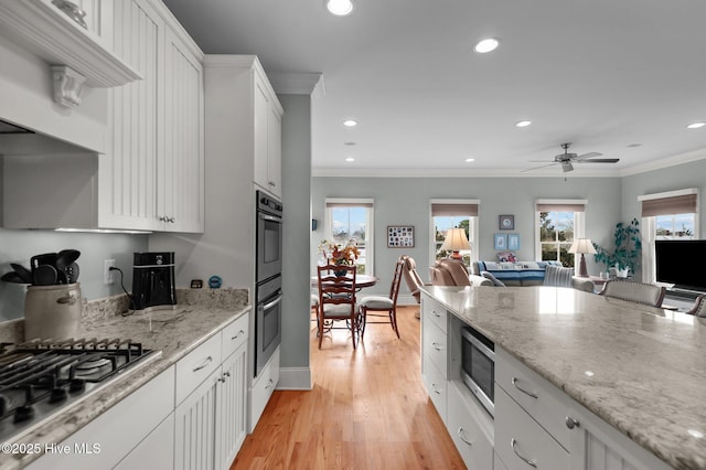 kitchen with crown molding, stainless steel appliances, open floor plan, white cabinets, and a healthy amount of sunlight