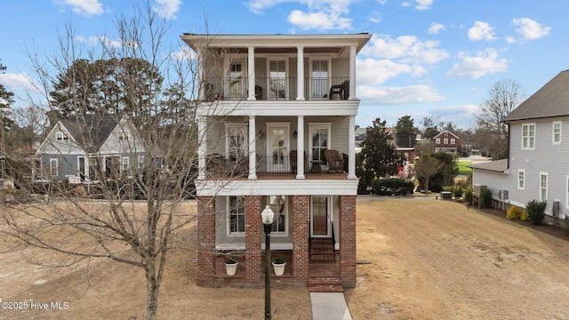 view of front facade with brick siding, a balcony, and dirt driveway