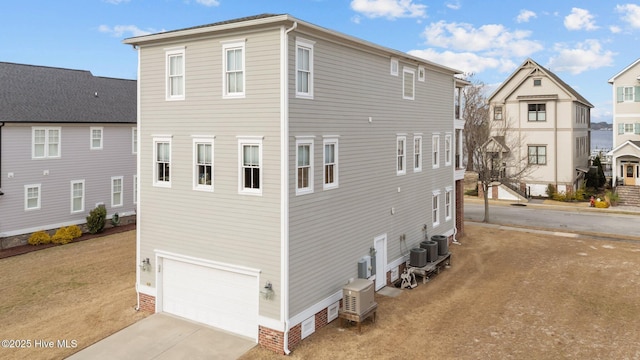 rear view of property with driveway, an attached garage, and central AC