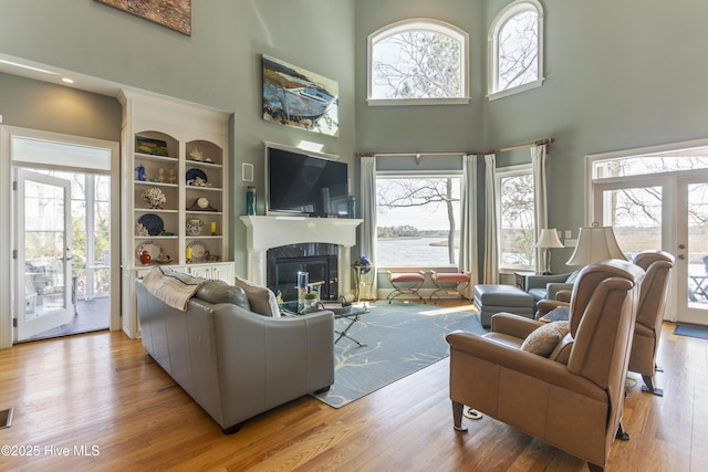 living room featuring french doors, wood finished floors, a high ceiling, and a glass covered fireplace