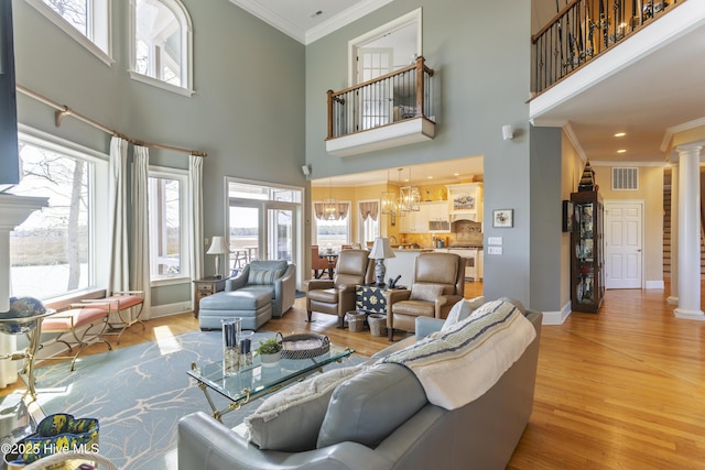 living room with visible vents, crown molding, a chandelier, wood finished floors, and ornate columns