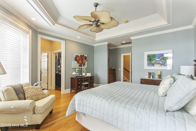 bedroom with a tray ceiling, light wood-style floors, ornamental molding, and a spacious closet