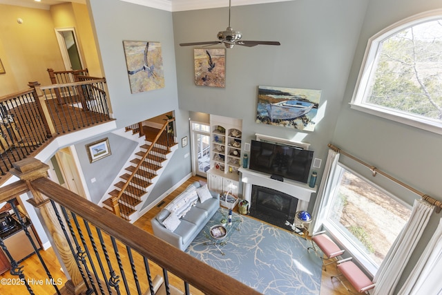 living room featuring baseboards, a fireplace with flush hearth, a towering ceiling, wood finished floors, and a ceiling fan