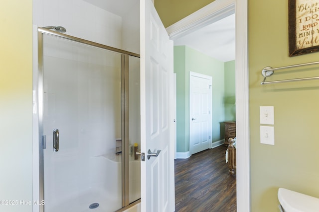 bathroom featuring a shower stall, toilet, wood finished floors, and baseboards