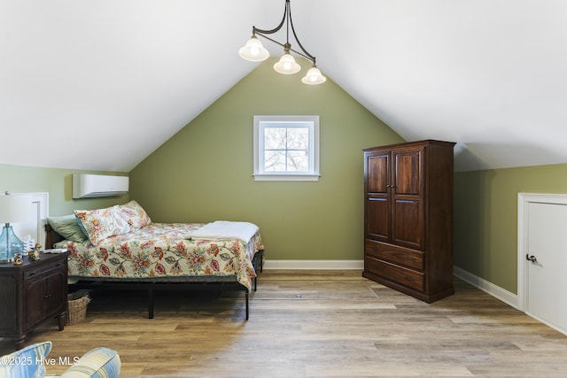 bedroom with light wood-style flooring, a wall mounted AC, baseboards, and vaulted ceiling