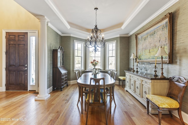 dining space featuring baseboards, ornate columns, light wood-style floors, a raised ceiling, and a notable chandelier