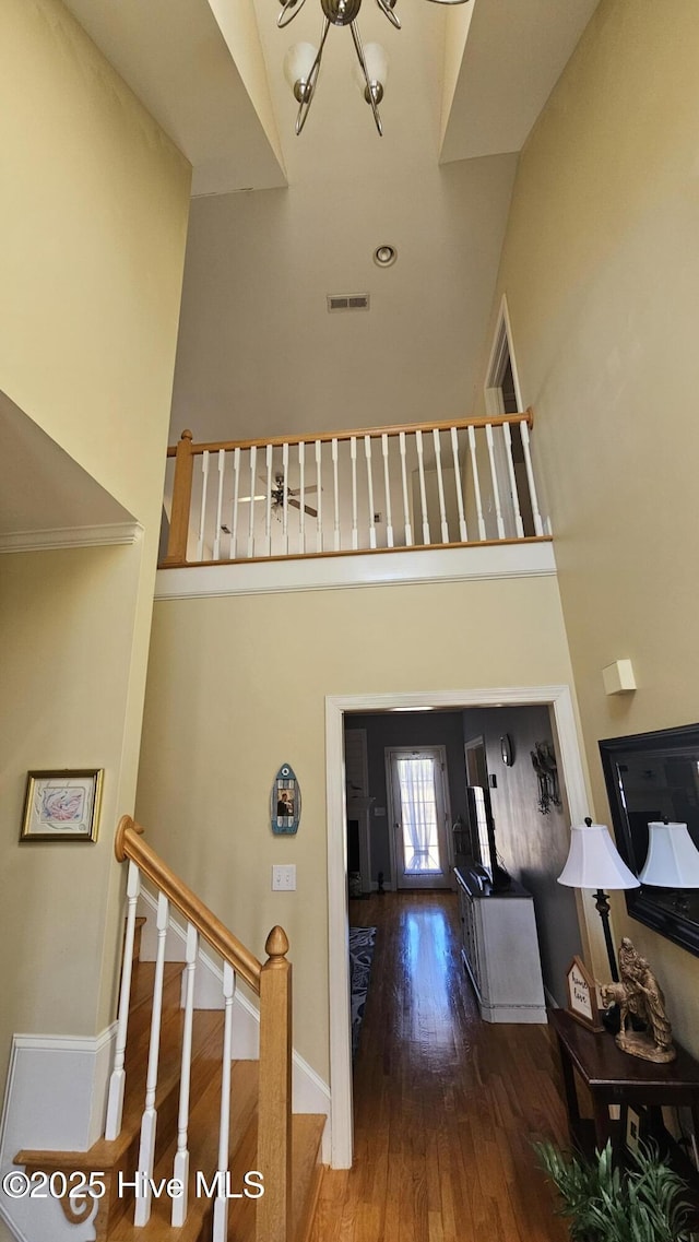 foyer entrance with wood finished floors, visible vents, a towering ceiling, baseboards, and stairway