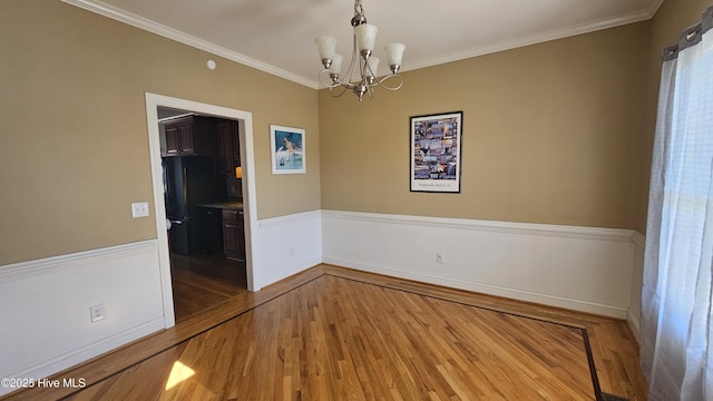 spare room featuring ornamental molding, a notable chandelier, and wood finished floors