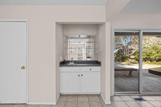 bar featuring light tile patterned floors, baseboards, indoor wet bar, and a sink