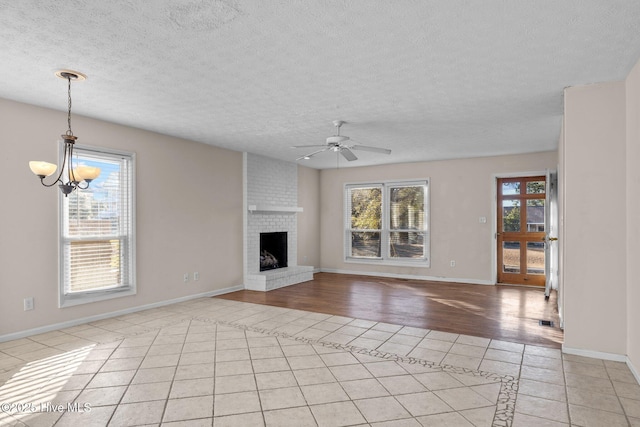 unfurnished living room with ceiling fan with notable chandelier, a wealth of natural light, a brick fireplace, and light tile patterned floors