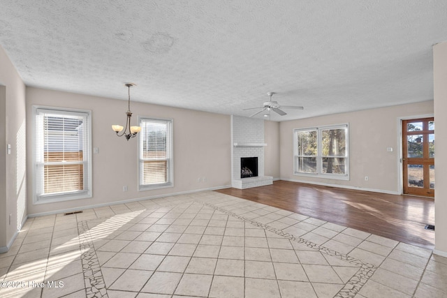 unfurnished living room featuring light tile patterned floors, ceiling fan with notable chandelier, a brick fireplace, and plenty of natural light