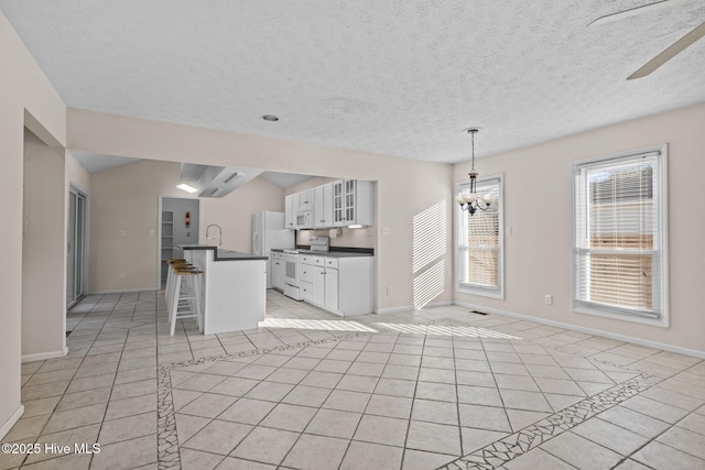 kitchen with white appliances, light tile patterned floors, dark countertops, a kitchen bar, and a chandelier